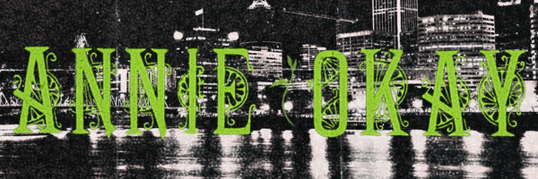 green stylized letters spelling annie okay in front of a beat up photo of Portland, Oregon
